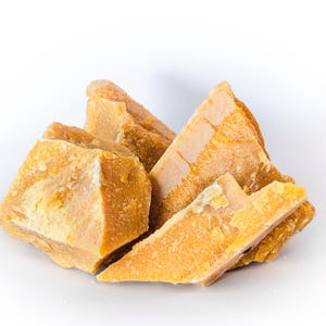 May include: A collection of irregularly shaped, golden-yellow beeswax blocks. The wax pieces have a rough, textured surface and vary in size, with some appearing triangular. The image is set against a clean white background, highlighting the natural color and texture of the wax.