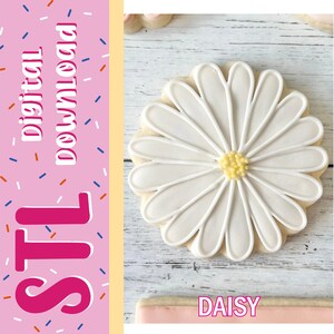Pode incluir: Um biscoito em forma de margarida com pétalas de glacê branco e centro amarelo, ao lado de uma barra lateral rosa com o texto digital download, STL e DAISY. O biscoito está sobre uma superfície de madeira clara com veios visíveis.