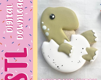 Può includere: Un biscotto a forma di cucciolo di dinosauro che esce da un uovo bianco con macchie nere. Il dinosauro è verde salvia con un occhio bianco e piccoli punti bianchi sulla testa. L'immagine include il testo digital download, STL e DINOSAUR HATCH.
