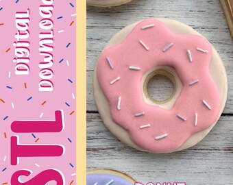 Può includere: Un biscotto rotondo a forma di ciambella con glassa rosa e piccoli zuccherini bianchi e azzurri. L'immagine include un pannello laterale rosa con il testo digital download e STL, e la parola DONUT è stampata vicino all'angolo in basso a destra.