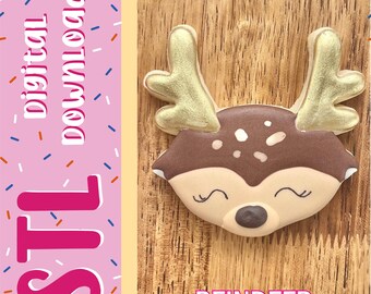 Può includere: Un biscotto a forma di renna con glassa marrone e beige, corna dorate e occhi chiusi. Il lato sinistro presenta un pannello rosa con zuccherini colorati e il testo "digital download" e "STL" in bianco e rosa, con "REINDEER" in basso.