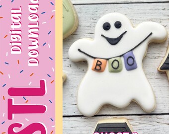 Può includere: Un biscotto bianco a forma di fantasma con occhi e bocca neri, che tiene un filo con tre piccole bandiere quadrate arancioni, verdi e viola che compongono la parola BOO. L'immagine include il testo rosa digital download STL.