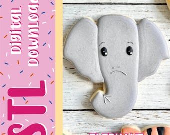Può includere: Un biscotto grigio a forma di elefante con occhi neri e una piccola bocca. Il lato sinistro presenta una fascia verticale rosa con il testo "digital DOWNLOAD" e "STL" in bianco e rosa. La parola "ELEPHANT" è stampata in rosa in basso.