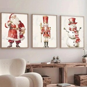 May include: Three framed watercolour paintings depicting Christmas characters. The first painting features Santa Claus in a red suit with a white beard. The second painting features a toy soldier in a red and gold uniform. The third painting features a snowman wearing a red and white scarf.