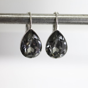 Puede incluir: Un par de pendientes de plata con piedras de cristal negras en forma de lágrima.