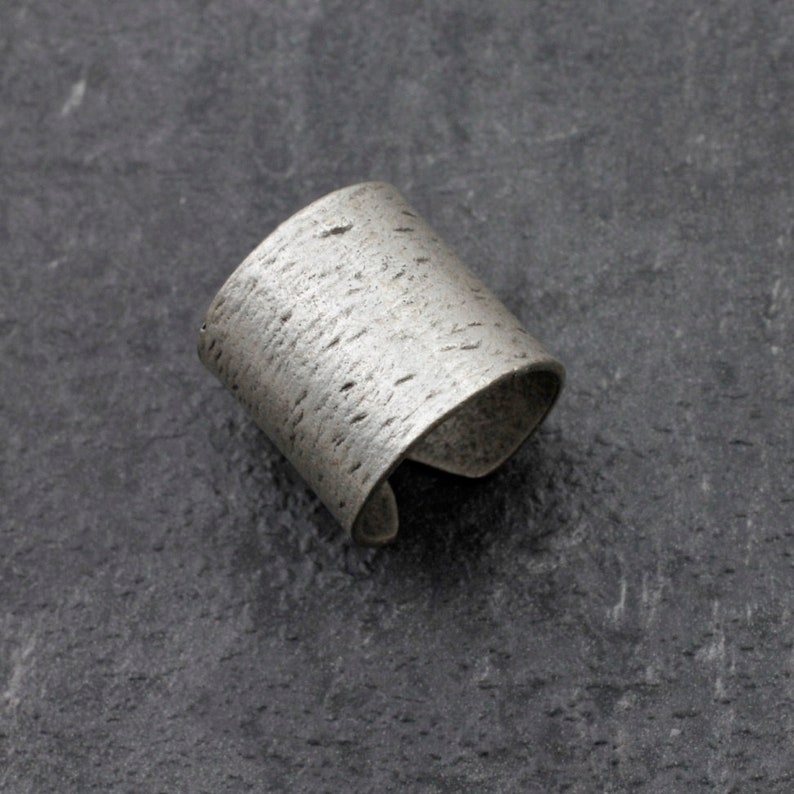 Puede incluir: Un brazalete de plata con una superficie texturizada.