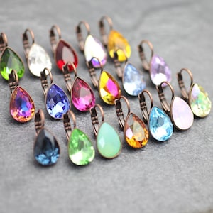Puede incluir: Una colección de 18 pendientes de cristal en forma de lágrima en varios colores, incluidos azul, verde, rojo, naranja, amarillo y morado. Los pendientes están unidos a ganchos de palanca de color cobre.