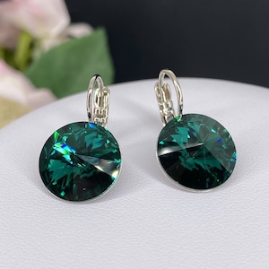 May include: A pair of silver hoop earrings with emerald green crystal stones. The earrings have a simple design and are perfect for everyday wear.