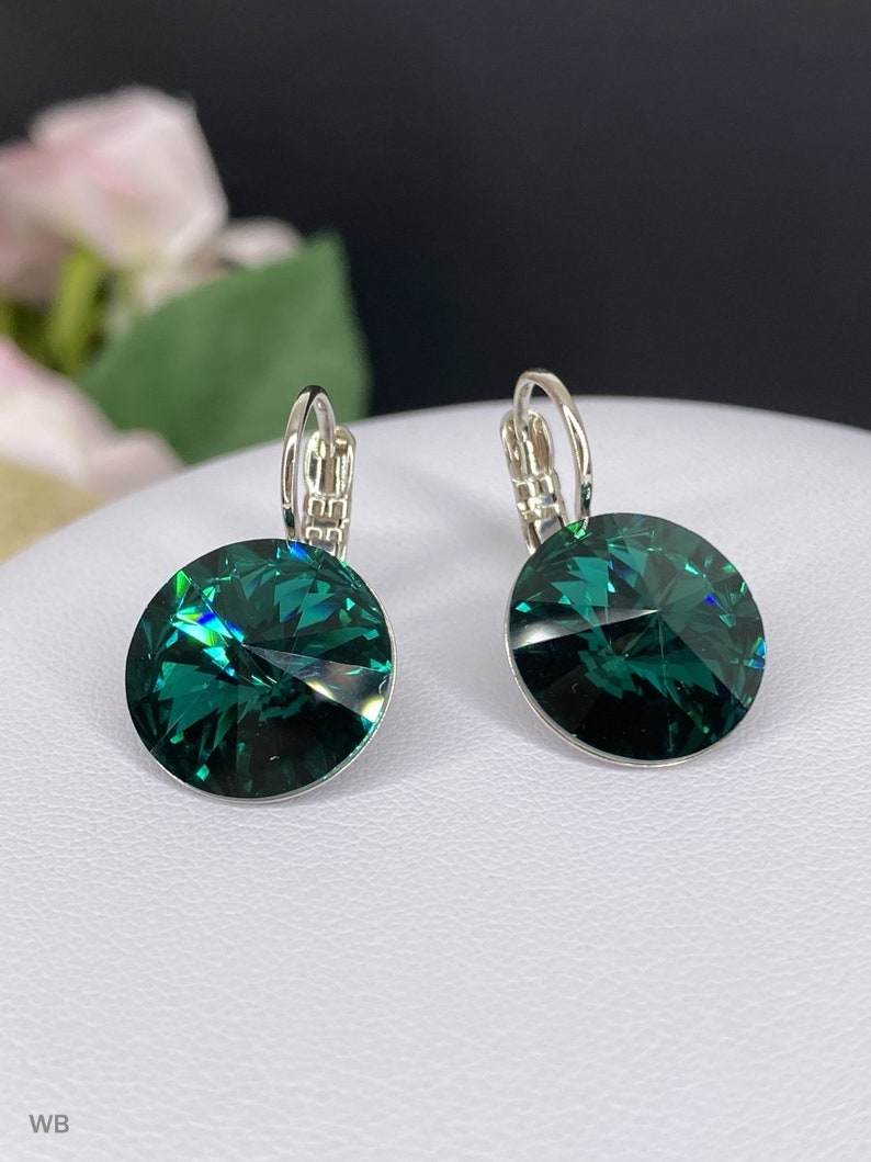 May include: A pair of silver hoop earrings with emerald green crystal stones. The earrings have a simple design and are perfect for everyday wear.