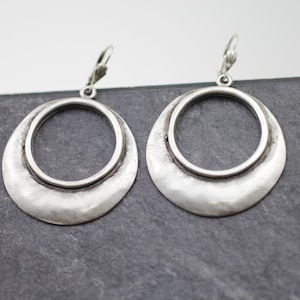Può includere: Un paio di orecchini a cerchio in argento con finitura martellata. Gli orecchini hanno una forma rotonda grande con un cerchio più piccolo all'interno.