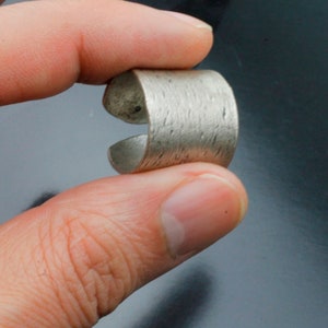 Puede incluir: Un anillo de plata con una superficie texturizada. El anillo est&aacute; abierto por un lado y tiene una banda ancha.