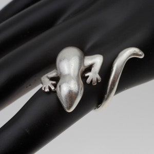 May include: A silver ring shaped like a lizard with a curled tail.