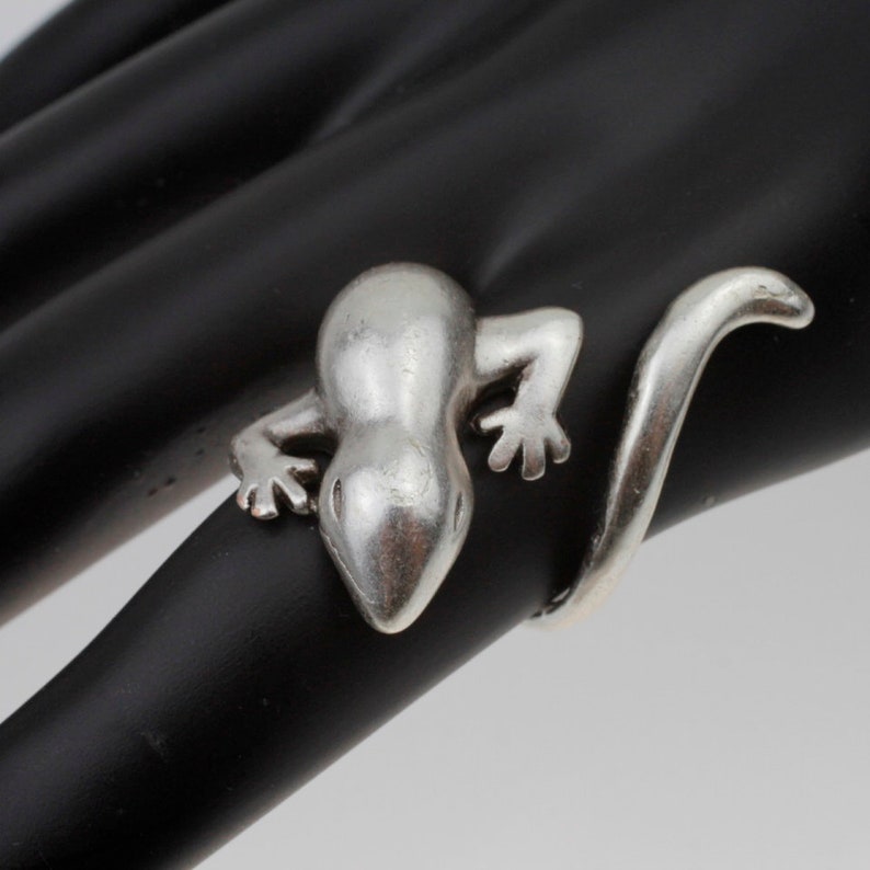 May include: A silver ring shaped like a lizard with a curled tail.