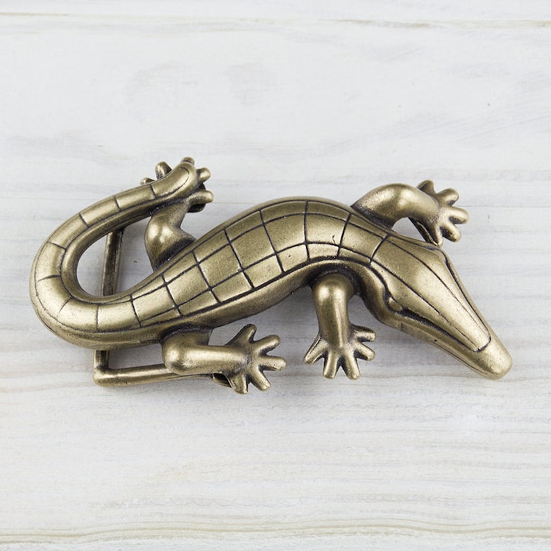 May include: A gold-toned metal belt buckle shaped like an alligator. The buckle has a detailed design with scales and claws.