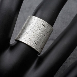 Puede incluir: Un anillo ancho de plata con una superficie texturizada.