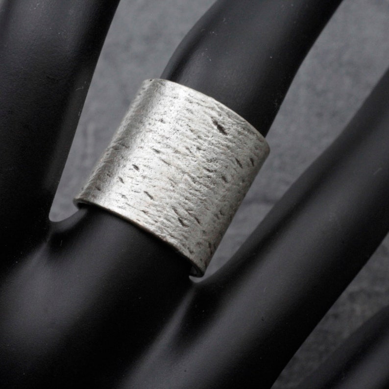 Puede incluir: Un anillo ancho de plata con una superficie texturizada.