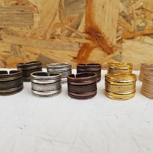 Könnte beinhalten: Acht Metallringe mit verschiedenen Mustern und Oberflächen. Die Ringe sind silber, gold, bronze und kupferfarben.