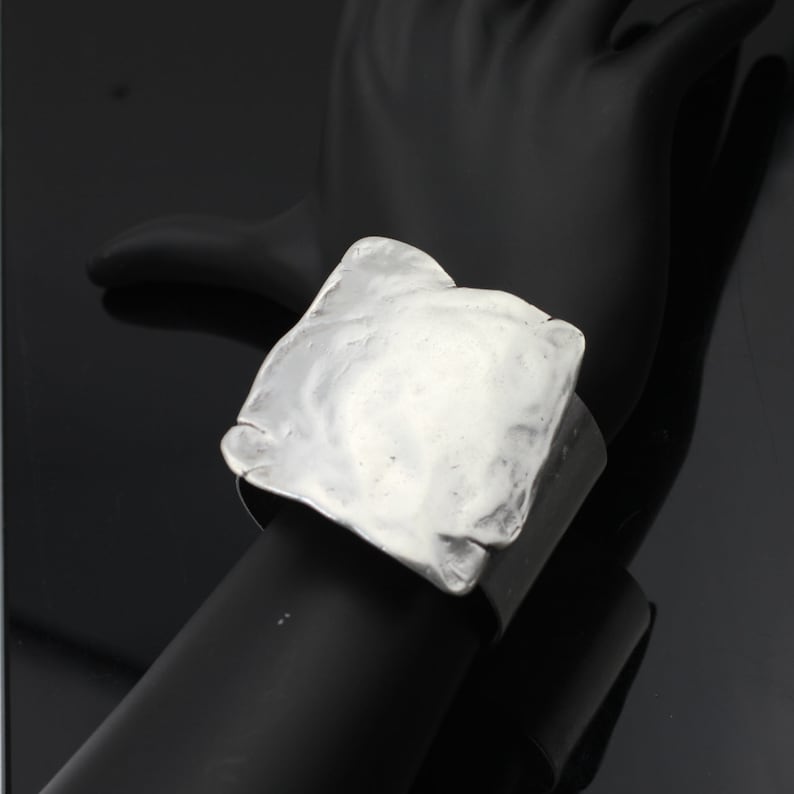 Op de afbeelding: Een zilveren vierkante armband met een getextureerd oppervlak.