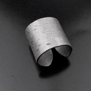 Puede incluir: Un anillo de plata con una superficie texturizada que se asemeja a la corteza de abedul.