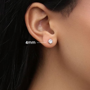 Könnte beinhalten: Nahaufnahme eines Ohrs mit einem kleinen, runden, durchsichtigen Ohrstecker. Der Ohrring hat einen Durchmesser von ca. 4 mm. Der Ohrring ist in einer Metalleinfassung gefasst und funkelt.