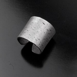 Puede incluir: Un anillo de plata con una superficie texturizada. El anillo est&aacute; abierto y tiene una banda ancha.