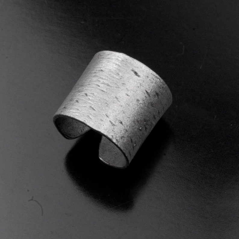 Puede incluir: Un anillo de plata con una superficie texturizada. El anillo est&aacute; abierto y tiene una banda ancha.