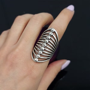 Peut inclure: Une bague en argent avec un design géométrique composé d'une série de lignes courbes et de petites perles rondes.