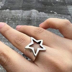 Puede incluir: Un anillo de plata con un diseño en forma de estrella. La estrella es hueca y tiene un borde puntiagudo.