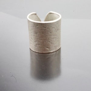 Puede incluir: Un anillo de plata con un acabado texturizado y martillado. El anillo es ancho y tiene una forma ligeramente redondeada.