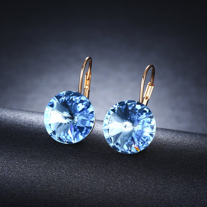 May include: A pair of gold-tone earrings with light blue crystal accents. The earrings have a simple, elegant design.