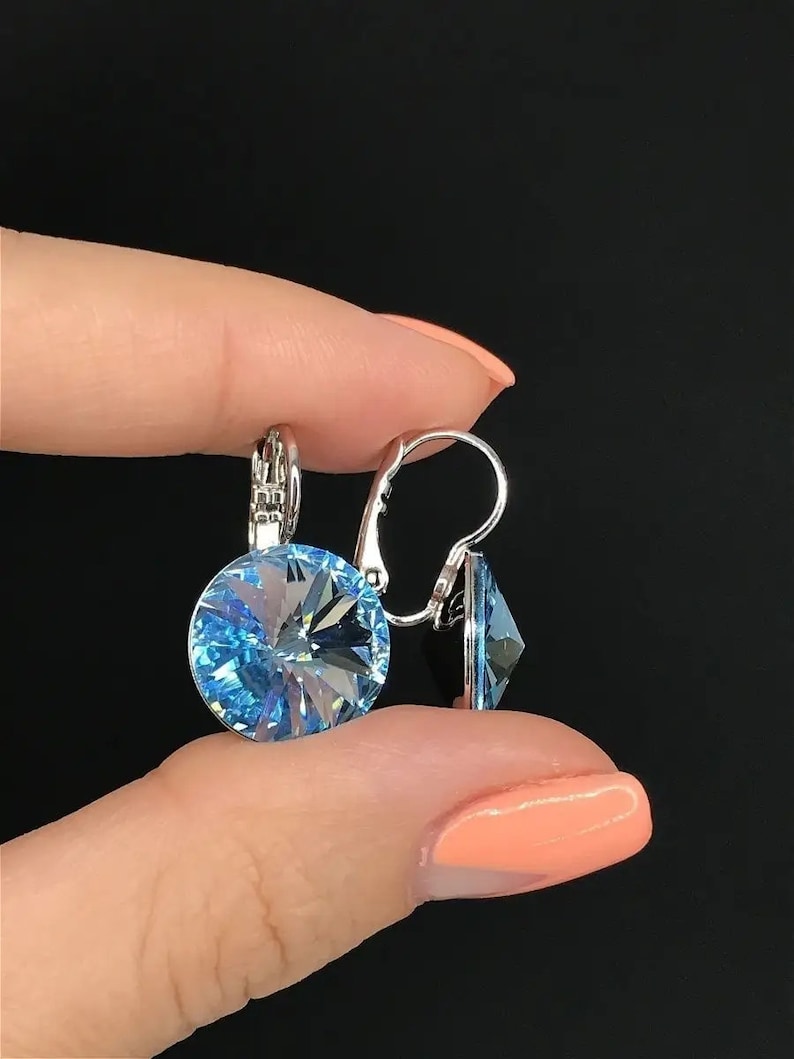 May include: A pair of silver earrings with light blue crystal stones. The earrings have a simple design and are perfect for everyday wear.
