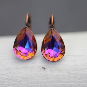 Puede incluir: Un par de pendientes en forma de lágrima con un engaste de metal color cobre. Los cristales facetados muestran un vibrante degradado de color, que va del naranja al morado y al azul. Un accesorio elegante.