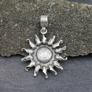 May include: Silver pendant in the shape of a stylized sun with a textured center and radiating rays.