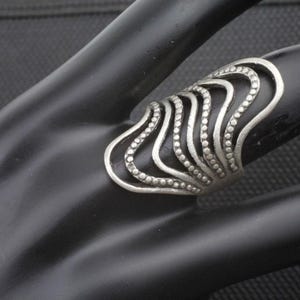 Puede incluir: Un anillo de plata con un diseño ondulado y en capas. El anillo está decorado con pequeñas cuentas redondas.