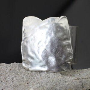 Op de afbeelding: Een zilveren ring met een getextureerde, vierkante band.