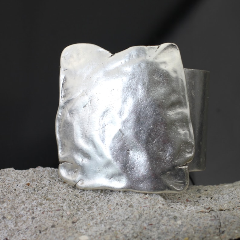 Op de afbeelding: Een zilveren ring met een getextureerde, vierkante band.