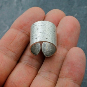 Puede incluir: Un anillo de plata con un acabado texturizado. El anillo est&aacute; abierto por un lado y tiene una forma ligeramente curvada.