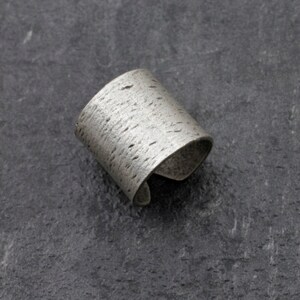 Puede incluir: Un brazalete de plata con una superficie texturizada.
