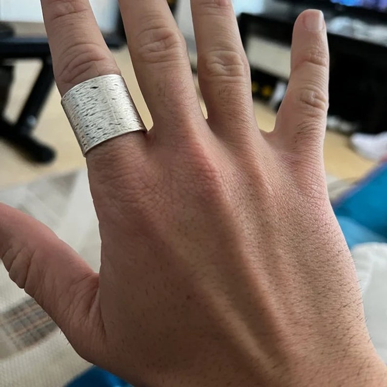 Puede incluir: Un anillo de plata texturizado usado en un dedo.