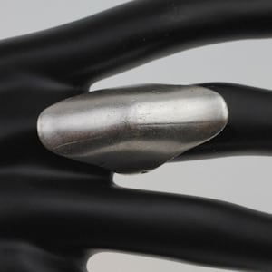 May include: A silver-toned ring with a wide, curved band. The ring is made of metal and has a smooth, polished finish.