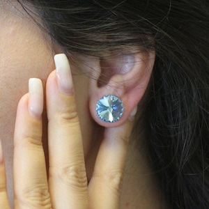 May include: A pair of blue crystal earrings. The earrings are round and have a faceted design. They are worn in a person's ear.