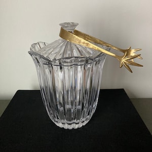 Peut inclure: Un seau à glace en verre transparent avec un motif cannelé et un couvercle et des pinces en métal doré.