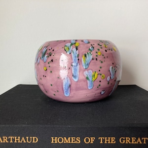 May include: A pink ceramic bowl with a speckled glaze and blue, green, and yellow abstract designs.