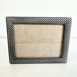 May include: A rectangular silver-toned picture frame with a textured, diamond-patterned border. The frame has a neutral-colored backing and is designed to hold a photograph or artwork. The frame is displayed on a white surface.