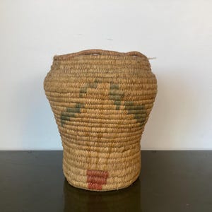 May include: A woven basket with a brown, tan, and green pattern. The basket is made of natural materials and has a round shape.