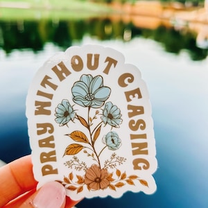 May include: A white sticker with a brown floral design and the text "Pray Without Ceasing" in brown lettering.