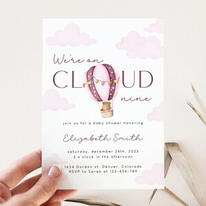 May include: Pink and brown baby shower invitation with a watercolor illustration of a hot air balloon with a teddy bear inside. The text reads "We're on CLOUD nine" and includes details for the event, such as the date, time, and location.