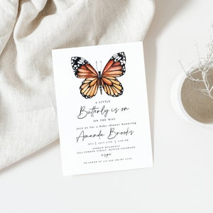 May include: A baby shower invitation featuring a watercolour illustration of an orange and black butterfly. The text reads "A Little Butterfly is on the Way" and includes the name "Amanda Brooks".