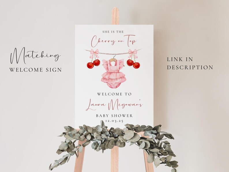 Puede incluir: Un cartel de bienvenida blanco con el texto "She is the Cherry on Top" en letra cursiva negra. El cartel tambi&eacute;n incluye un body de beb&eacute; rosa con una cereza en la parte superior, y el texto "Welcome to Laura McGowan's Baby Shower 12.03.25" en negro.