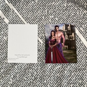 May include: A fantasy illustration of King Arthur and Queen Guinevere standing in front of a castle. Guinevere is wearing a red gown and holding a sword. Arthur is wearing a leather kilt and has his arm around Guinevere. The text "King Arthur & Guinevere A Loyal Betrayal" is at the bottom of the image.